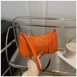 Detalle de bolso de charol naranja brillante con lazo dorado en un estante moderno liso