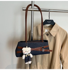 Detail of denim shoulder bag with leather straps and a cute plush bear keychain charm