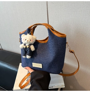Detail of blue denim shoulder bag with brown leather trim and cute teddy bear charm