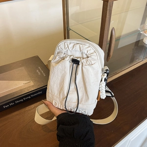 Minimalist beige nylon drawstring crossbody bag with embroidered logo and charm