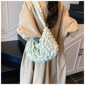 Detail of mint green puffy shoulder bag with ruched texture on a beige trench coat