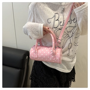 Pink polka dot cylinder bag shown on model with adjustable strap and top handle
