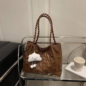 Brown faux leather tote bag with bear embossing and woven handles on a metal rack