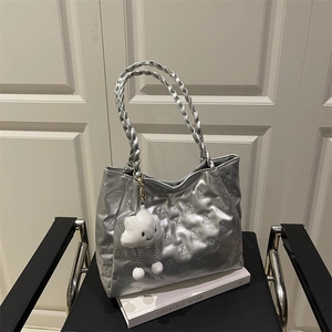 Chic silver metallic tote bag with bear quilting and plush cloud charm on a black chair