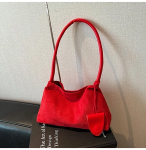 Λεπτομέρεια κόκκινης σουέτ τσάντας με κυλινδρική λαβή πάνω σε διακοσμητικό βιβλίο