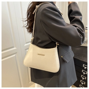 Détail du sac hobo crème avec barre dorée minimaliste sur une veste grise chic