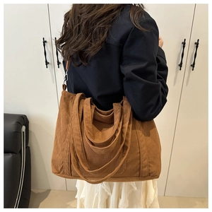 Brown corduroy tote bag with leather strap shown as a shoulder bag on a model