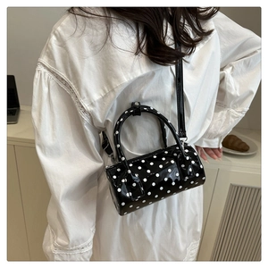 Polka dot cylinder bag shown on a model with dual handles and crossbody strap