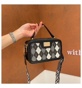 Detail of a black square crossbody bag featuring a classic plaid pattern and metal accent