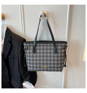 Detail of black gingham tote bag with golden logo lettering and metal ring accents