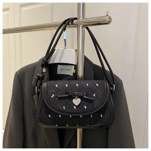 Detail of black pleated crossbody bag with white animal patterns and heart charm