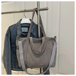 Close-up of grey corduroy tote bag with adjustable shoulder strap and front pocket detail