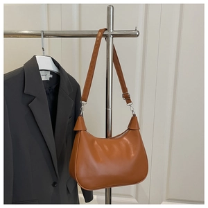 Detail of a brown leather crescent shoulder bag hanging next to a grey blazer on a hanger