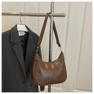 Detail of a brown vintage crescent moon bag hanging on a metal rack with a gray suit