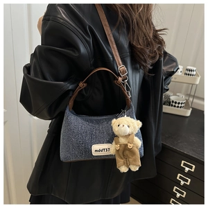 Detail of denim shoulder bag featuring a leather handle and a cute plush bear pendant