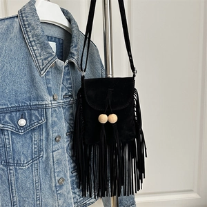 Borsa a tracolla retrò in camoscio nero con frange e perle in legno su sfondo in denim
