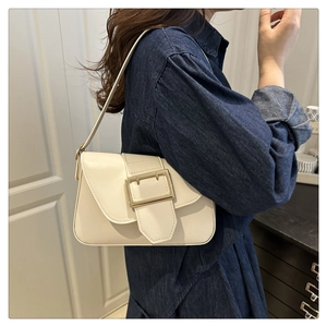 Detail of cream white shoulder bag featuring a large gold buckle and slim strap