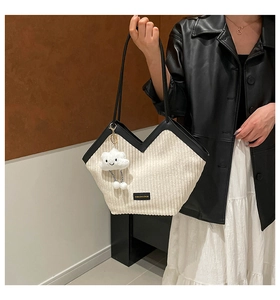 Detail of off-white corduroy tote bag with black V-trim and plush cloud charm accessory