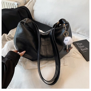Detail der schwarzen gefalteten Kunstledertasche mit weißem Plüsch-Anhänger und Prägung