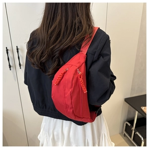 Detail of red nylon waist bag with woven zipper pullers and adjustable strap on a model