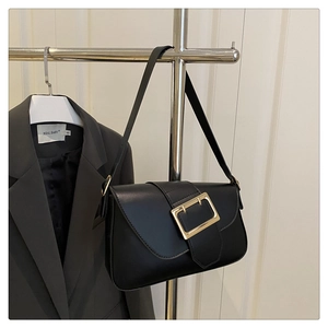 Close-up of black leather shoulder bag featuring a large rectangular gold metal buckle