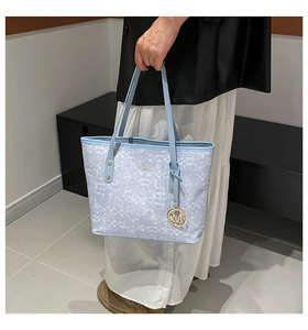 Detail of light blue checkered tote bag with gold M charm and reinforced handle rivets
