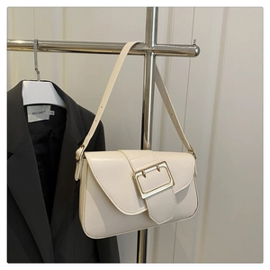 Detail of cream crossbody bag with large gold buckle and adjustable strap on a hanger