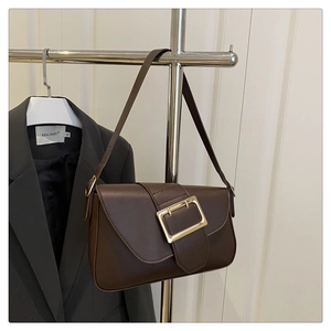 Detail of minimalist brown leather underarm bag featuring a large gold square metal buckle