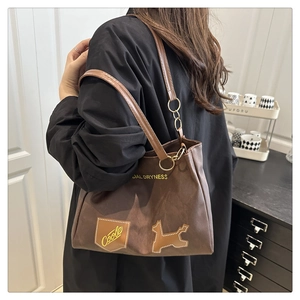 Detail of brown leather tote with dog patch and gold chain strap worn by a model