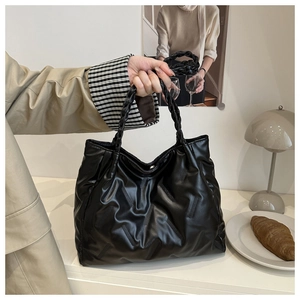 Detail of black quilted tote bag featuring woven handle and magnetic snap closure
