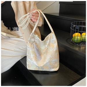 Detailed view of cream jacquard shoulder bag with golden embroidery and long grey tassel