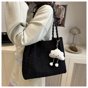 Detail of black woven shoulder bag with white cloud plush charm in a modern interior
