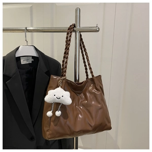 Macro detail of brown quilted leather tote bag with woven handle and cloud plush charm