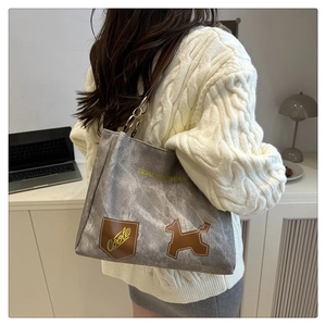 Detail of grey canvas tote bag with brown leather dog patch and metal ring on shoulder strap