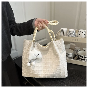 Detail of cream textured tote bag with woven handles and a cute cloud charm pendant