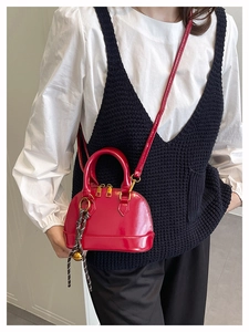 Close-up of bright red shell-shaped crossbody bag with gold zippers and woven charm