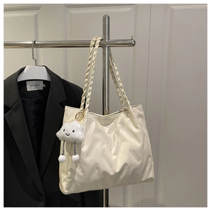 Detail of a beige quilted tote bag with a woven strap and a plush cloud charm decoration