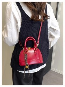 Detail of red shell handbag with gold hardware and woven metal ball charm accessory