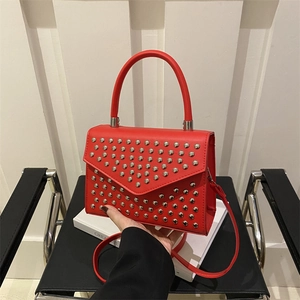 Elegant red leather handbag with silver rivets and V-flap, shown in hand for scale