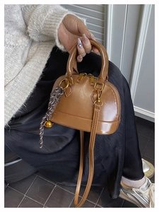 Detail of a brown shell handbag with gold hardware and a woven bell charm accessory
