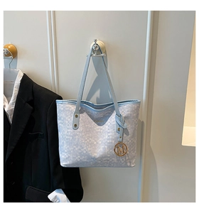 Dettaglio borsa tote azzurra con texture a griglia e ciondolo a M in metallo dorato