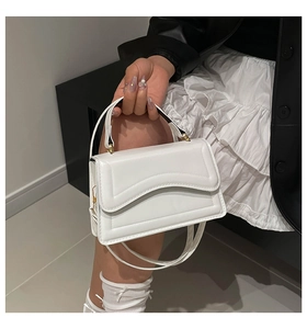 Detailed view of white crossbody bag with curved wave flap and golden hardware on model