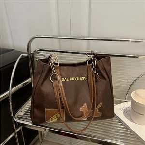 Brown canvas underarm tote bag with yellow letters and dog patch on a metal shelf