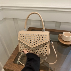 Minimalist beige crossbody bag with silver studs and top handle on a wooden table