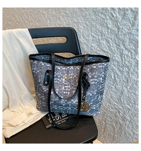 Dettaglio borsa shopper grigia pixelata con ciondolo M dorato su sedia nera minimalista