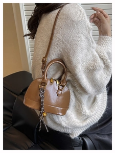 Detailed side view of a brown shell bag with braided knot pendant worn by a model