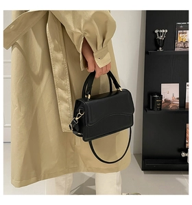 Detail of black leather shoulder bag with wavy flap design and gold metal buckle