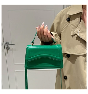 Detail of green crossbody bag with wavy flap design and gold hardware on a beige coat