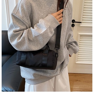 Model wearing a black nylon cylinder crossbody bag with adjustable straps in a casual setting