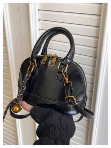 Detail of black patent leather shell bag featuring gold zippers and a woven bell charm